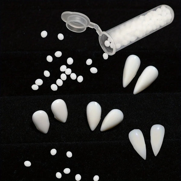 A collection of realistic resin vampire fangs in various sizes and shapes, some with adhesive gel, displayed on a black surfa