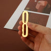 A hand holds a polished gold house number with a self-adhesive backing against a dark brown surface.