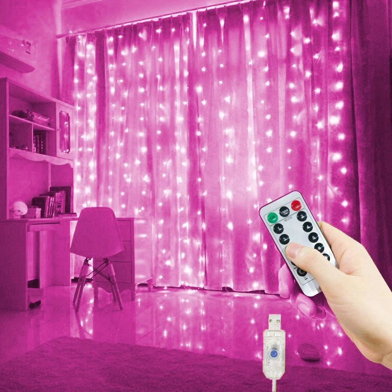 A hand holds a remote control for USB-powered LED curtain lights illuminating a pink room.