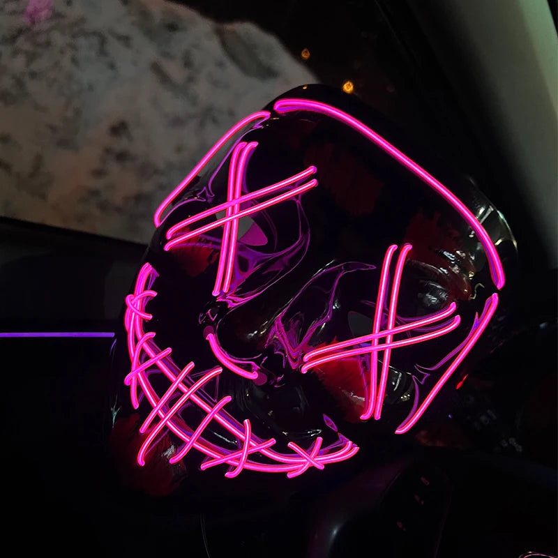 A close-up of a black mask with neon pink wire details, glowing in a dark interior setting.