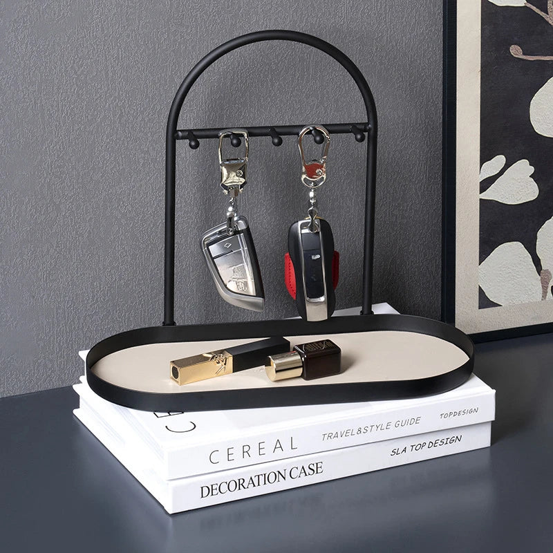 A black wrought iron desk organizer rack holding two silver pendant necklaces and a leather decoration case on a white stack 