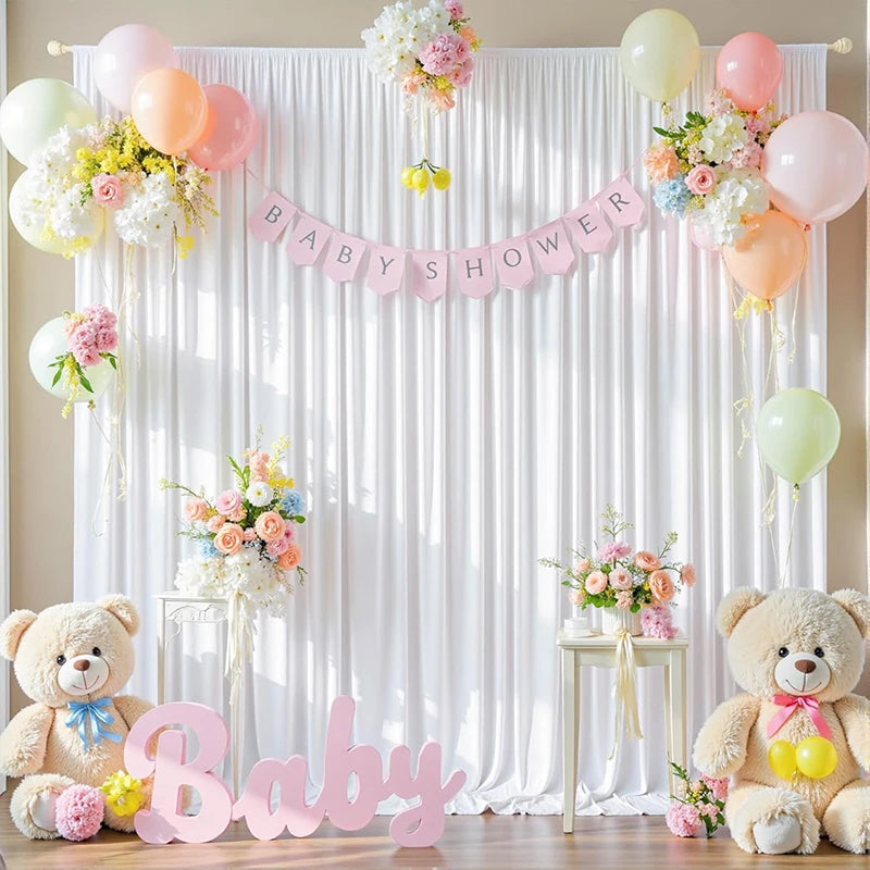 A pink and white fabric backdrop for a baby shower featuring floral arrangements and a large pink baby text