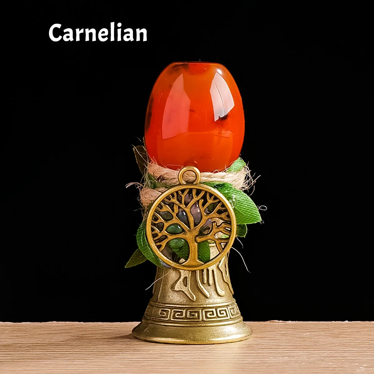 A smooth, orange-red Carnelian crystal sphere resting on a brass Tree of Life chime.