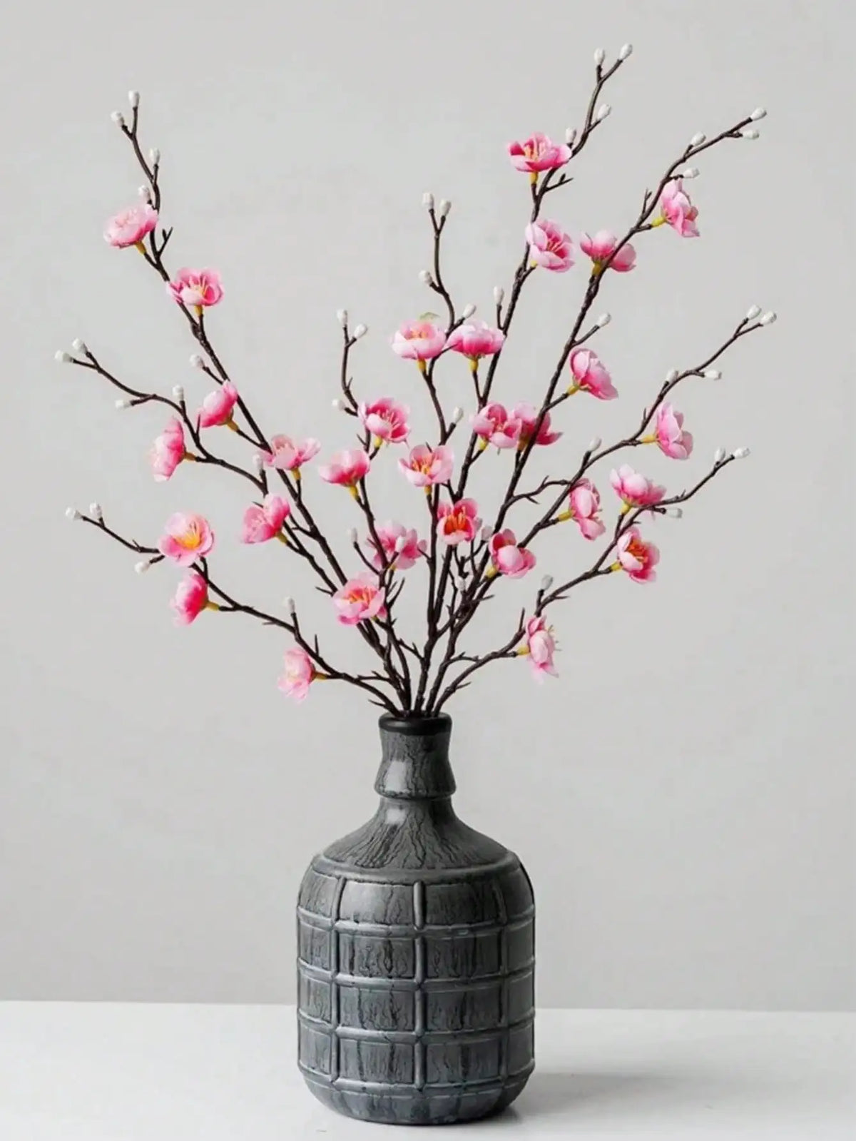 Ramitas de flor de ciruela blanca artificial en rosa y blanco en un jarrón gris oscuro