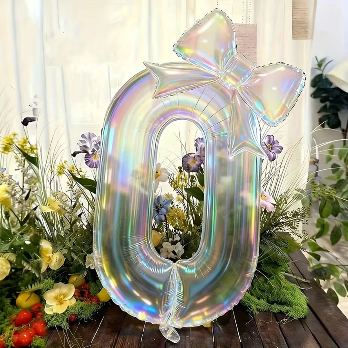 A large, iridescent, transparent number balloon shaped like the digit zero surrounded by greenery and flowers.