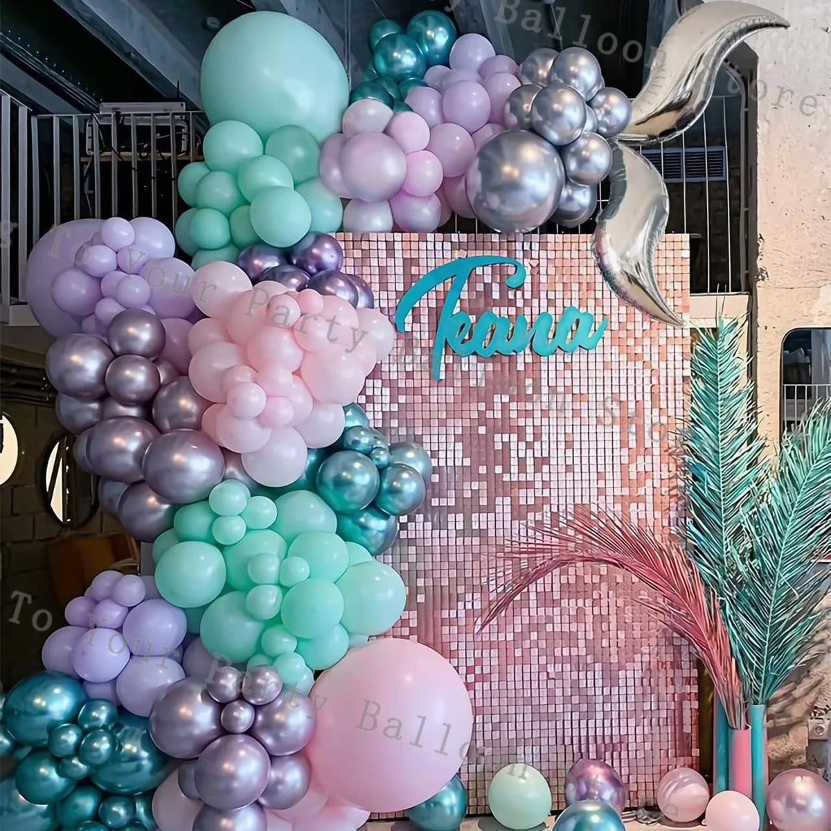A pastel balloon garland arch featuring shades of pink, purple, and teal clustered on a wooden backdrop.
