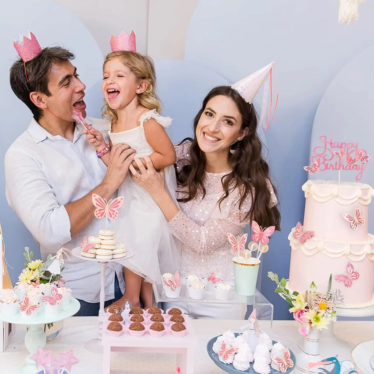 A family celebrating a birthday with pink butterfly cake toppers and tiered cakes.