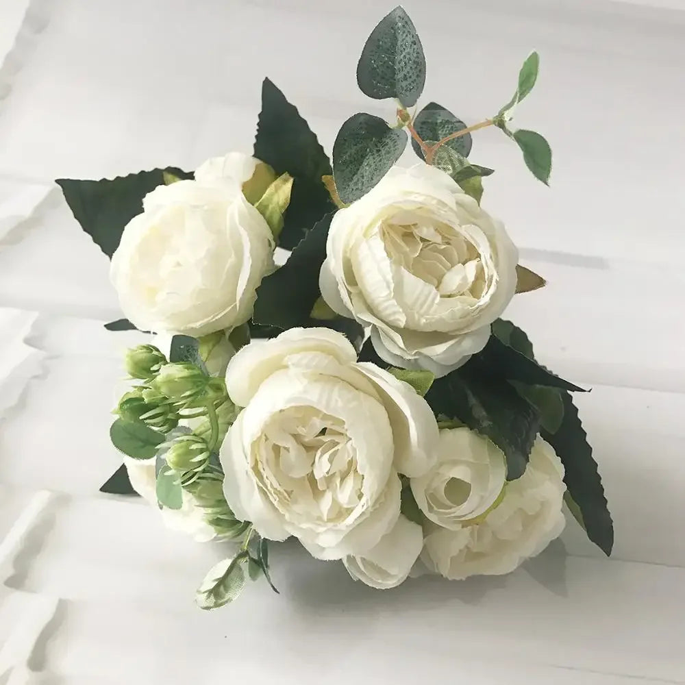 A bouquet of white silk roses and peonies with dark green foliage for home and event decor.