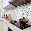 A kitchen countertop features a cooking pan on a stovetop below a white speckled wall and a stainless steel hood.