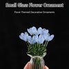 A hand holds a small glass flower ornament featuring light blue flowers in a clear glass vase.