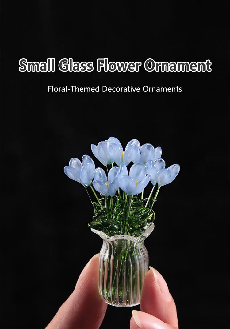 A hand holds a small glass flower ornament featuring light blue flowers in a clear glass vase.