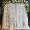 Elegant white wedding tulle backdrop decorated with cascading greenery and warm string lights
