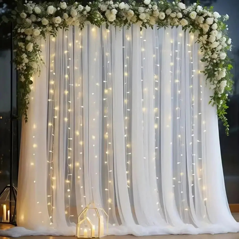 Elegant white wedding tulle backdrop decorated with cascading greenery and warm string lights