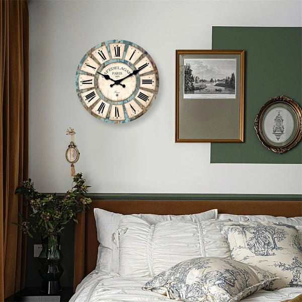 A rustic wooden wall clock with a distressed white face and Roman numerals hangs above a bed.