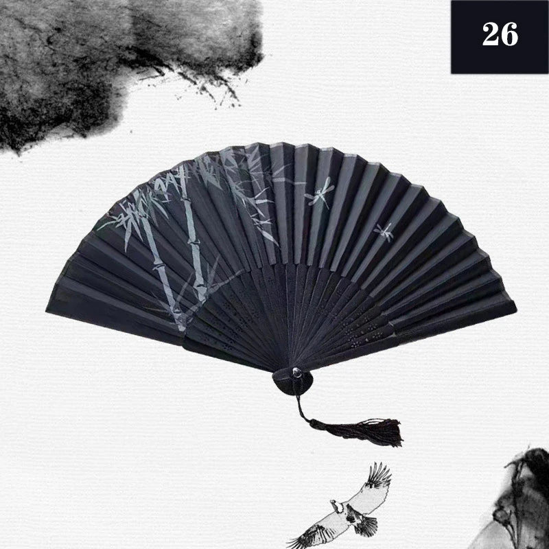 A black vintage silk bamboo folding hand fan with delicate white designs and a tassel.
