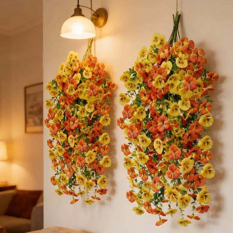 A vibrant hanging vine of artificial eucalyptus and violet pansy flowers displayed on a white wall.