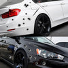 Close-up of a white car with bullet hole stickers on the side and a black car with similar decals on the headlight.