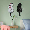 A black cat pendulum wall clock with a moving tail is mounted on a light green wall above a wooden desk.