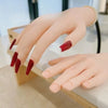 A hand model with long, red acrylic nails is displayed for manicure training.