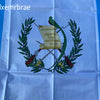 Guatemala National Flag displayed on white fabric with a green laurel wreath and text.