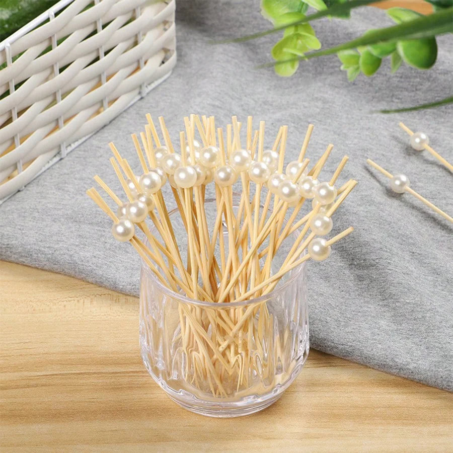 A glass container filled with bamboo fruit skewers adorned with pearl-like beads.