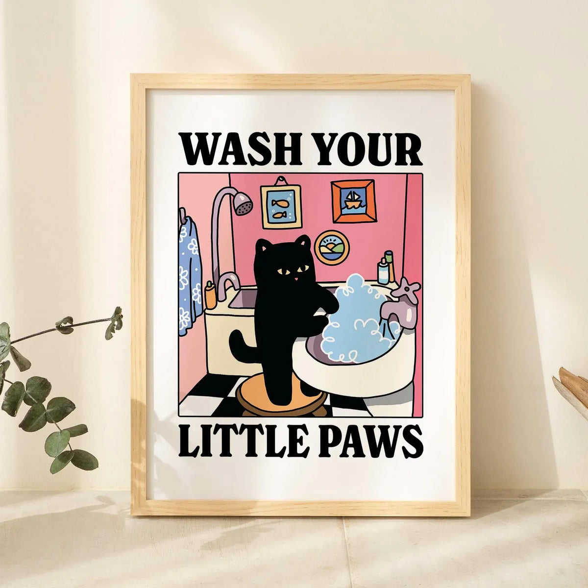 A framed poster with a watercolor illustration of a black cat washing itself in a bathtub, featuring the text Wash Your Littl