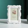 White ornate resin photo frame with a floral design displayed on a light green wall.