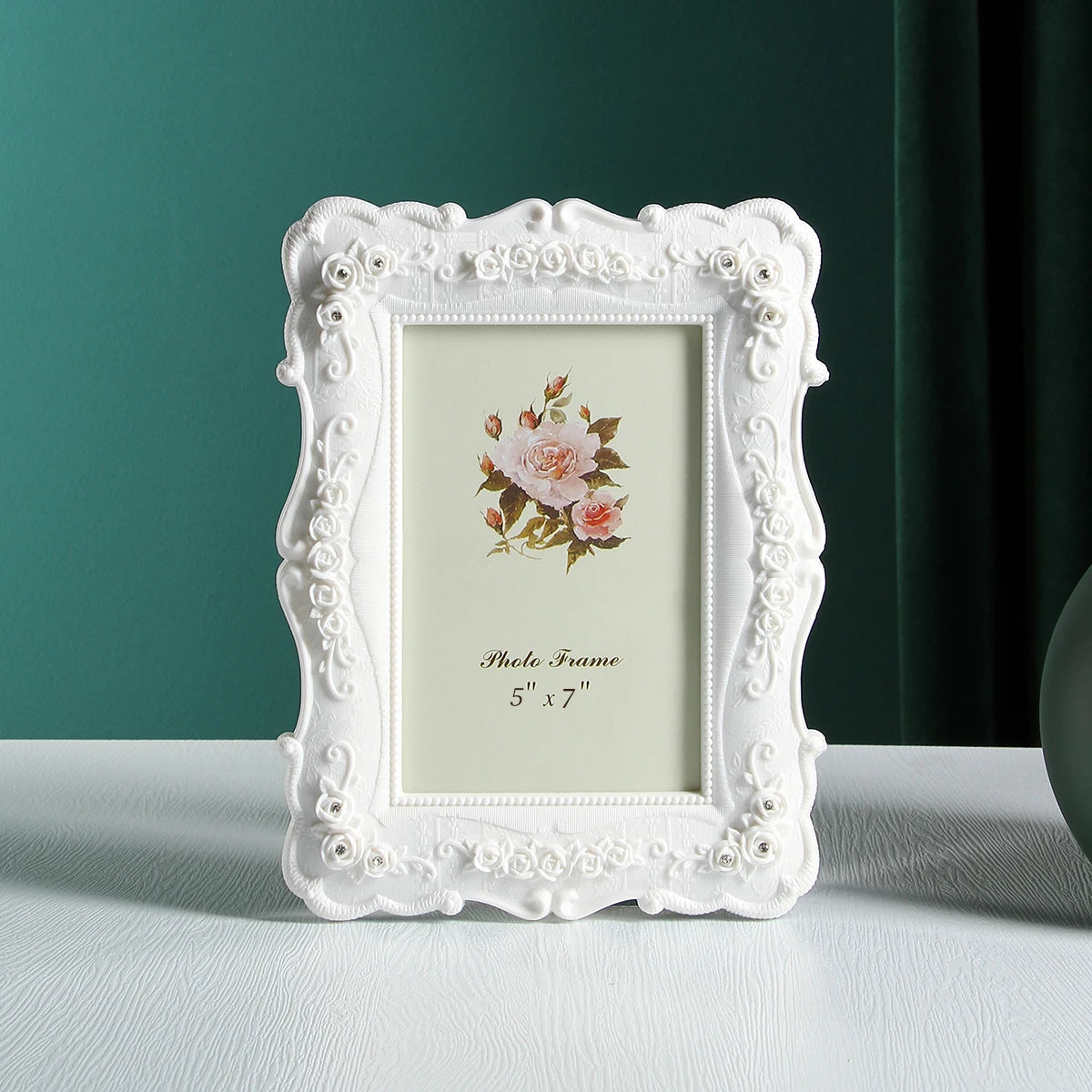 White ornate resin photo frame with a floral design displayed on a light green wall.