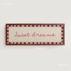 A framed canvas print with a light pink background and the text Sweet dreams in pink script on a white wall.