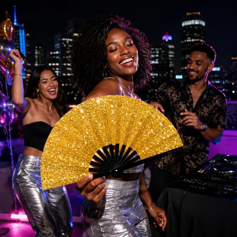 A woman in a black top and silver pants holds a large gold hand fan against a city skyline at night.