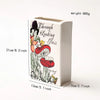 A white ceramic book-shaped vase featuring a botanical illustration of a fungus and text.