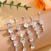 A set of five gold tone butterfly and flower belly rings with clear stones displayed on a beige surface.