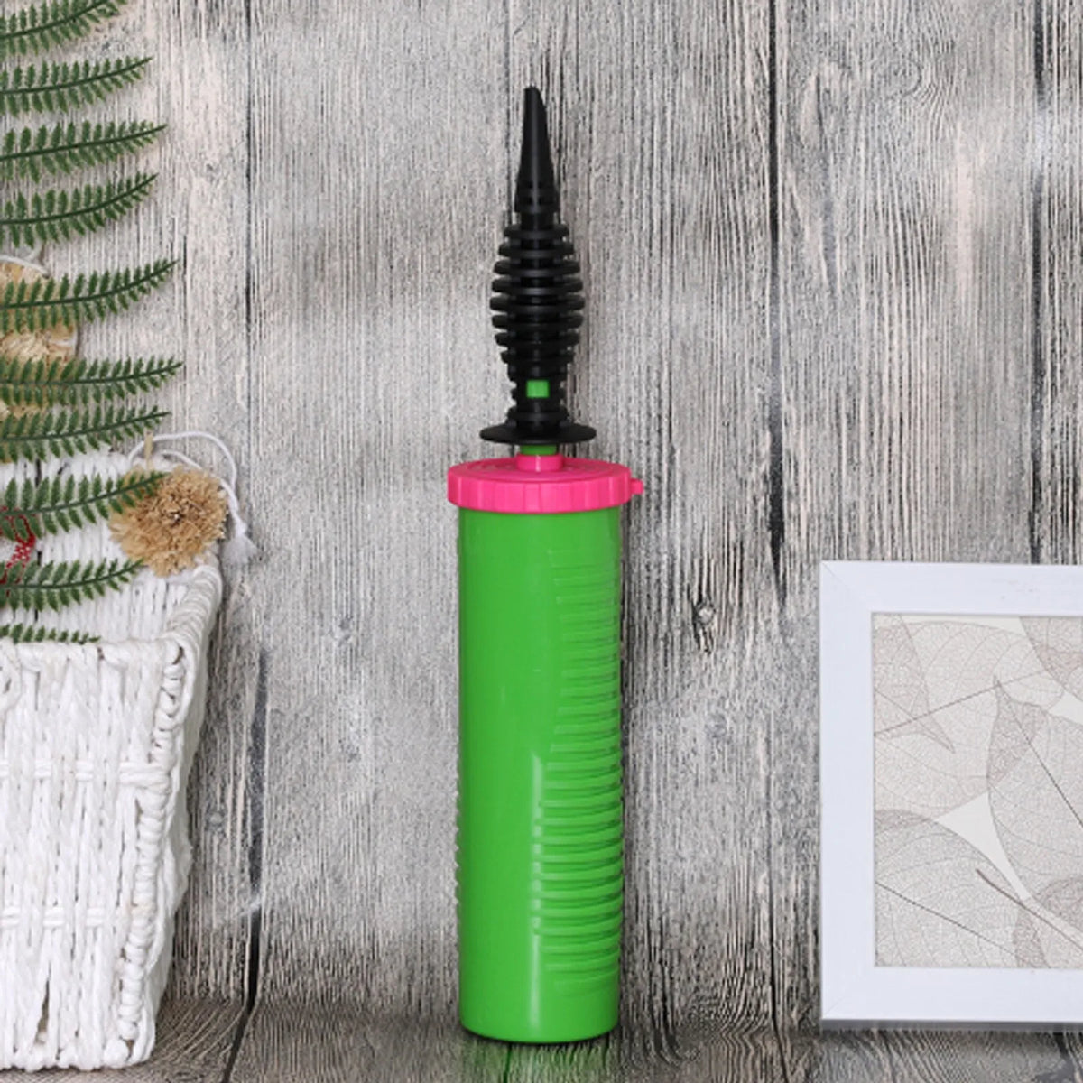 A bright green handheld balloon air pump with a black nozzle is shown against a rustic wooden background.