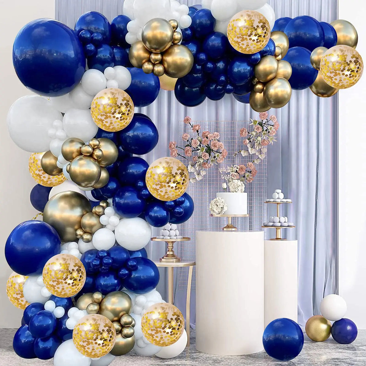 A balloon garland arch featuring navy blue, silver, gold, and white balloons displayed against a light blue curtain.