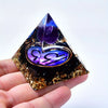 A hand holds a dark pyramid crystal with purple and gold decorative elements, representing twelve zodiac signs.