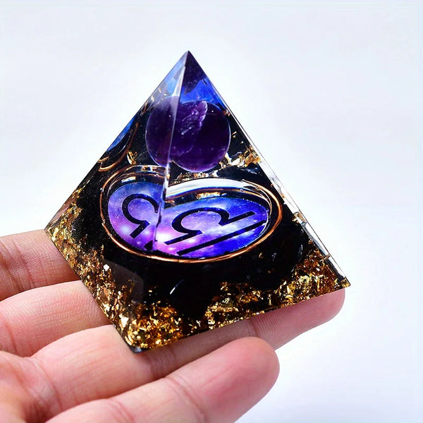 A hand holds a dark pyramid crystal with purple and gold decorative elements, representing twelve zodiac signs.
