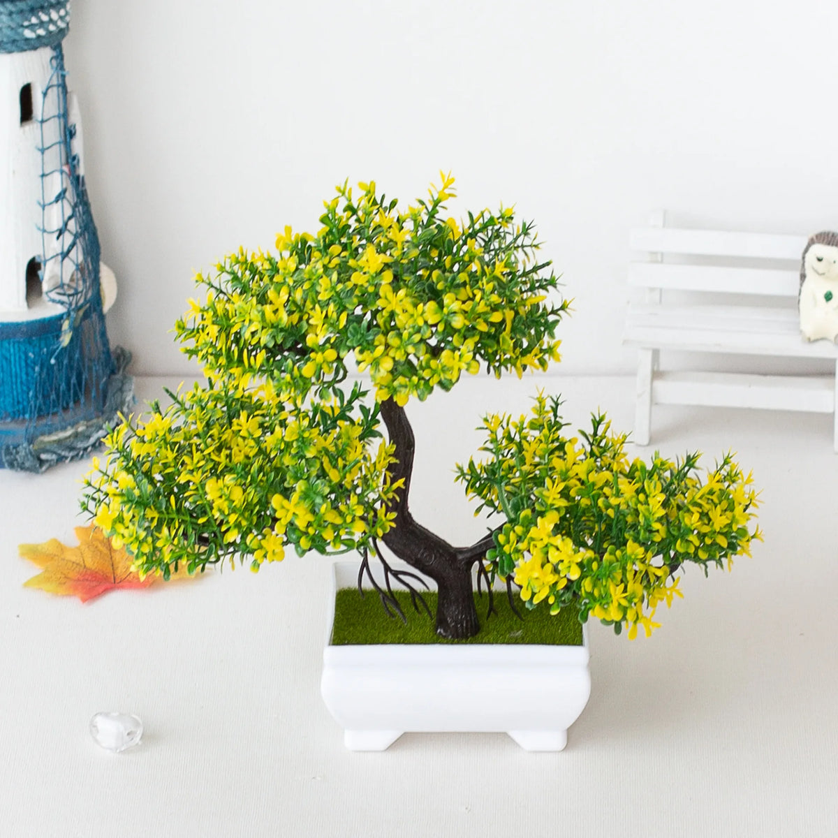 Un petit arbre bonsaï artificiel aux feuilles jaunes vives, exposé dans un pot rectangulaire blanc.