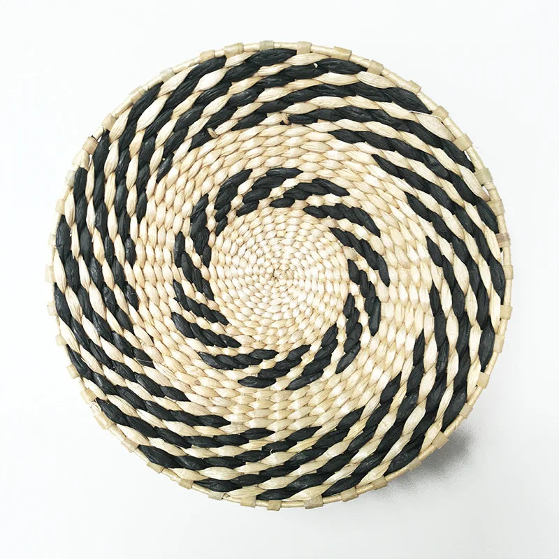 A round woven straw wall decor hanging with black and natural beige stripes in a spiral pattern.
