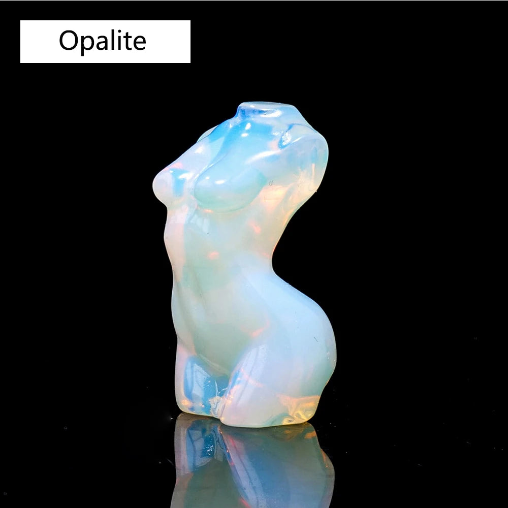 Figura de opalita azul pálido y translúcido con forma de torso femenino, reflejando luz en una superficie oscura.