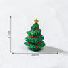 A small, green resin Christmas tree charm with a gold star topper resting on a white surface.