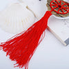A bright red tassel with a gold coin charm is displayed next to a white seashell on a light-colored book.