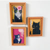 Dos retratos de punto de aguja enmarcados de gatos en blanco y negro con ojos rosa y blanco.