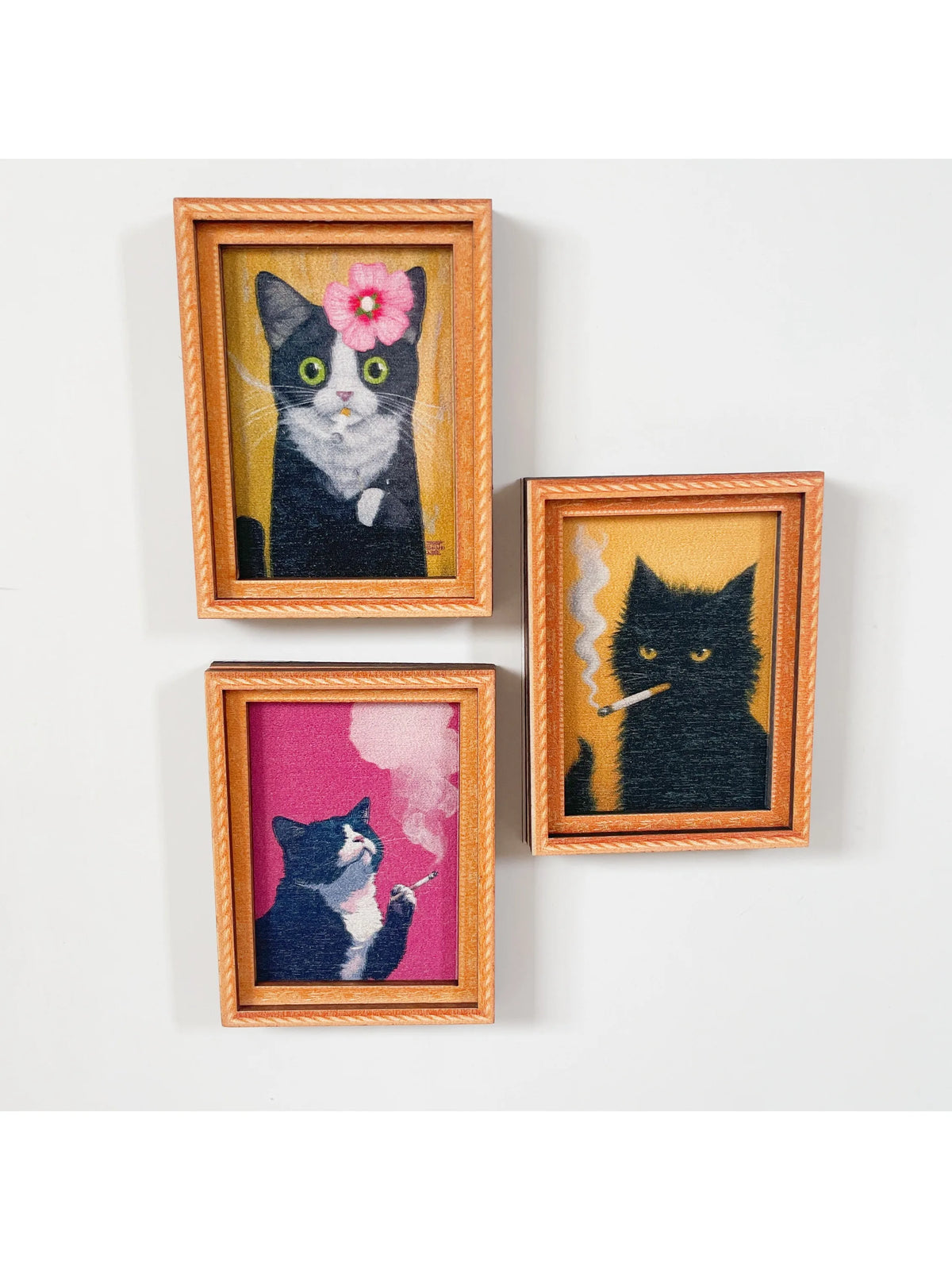Dos retratos de punto de aguja enmarcados de gatos en blanco y negro con ojos rosa y blanco.