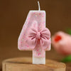 Vela número 4 rosa con lazo rosa sobre una superficie de madera.