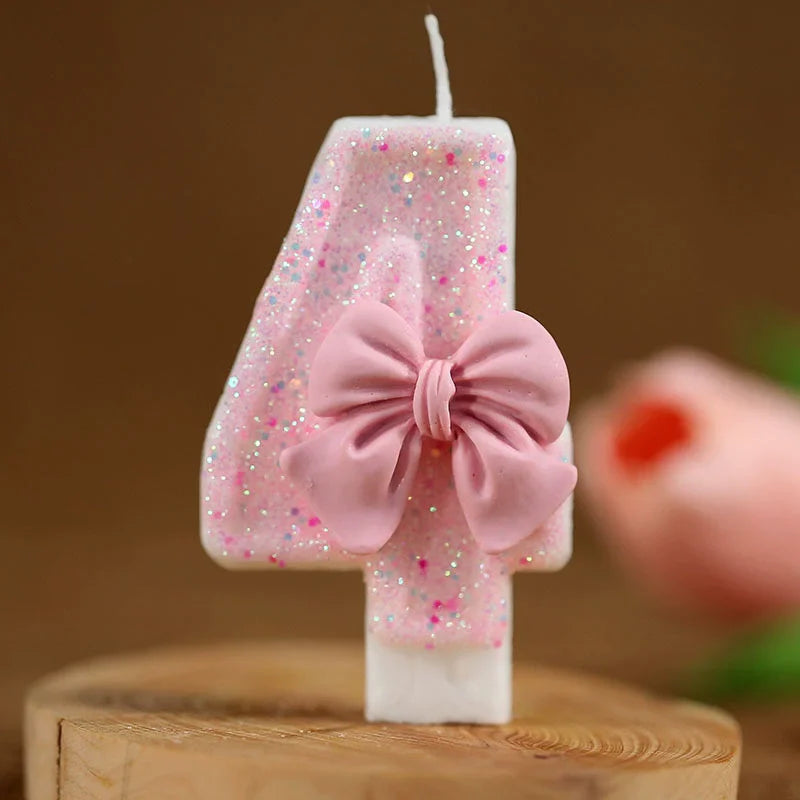 Vela número 4 rosa con lazo rosa sobre una superficie de madera.