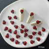 A collection of 50 ladybug shaped resin nail art charms displayed on a white ceramic plate.