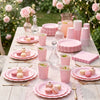 A wooden table set for an elegant pink scalloped paper tableware display with pink cups plates and cutlery.