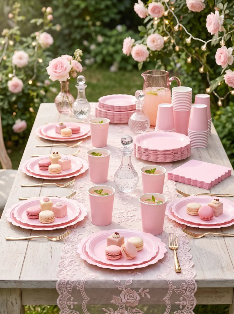 A wooden table set for an elegant pink scalloped paper tableware display with pink cups plates and cutlery.