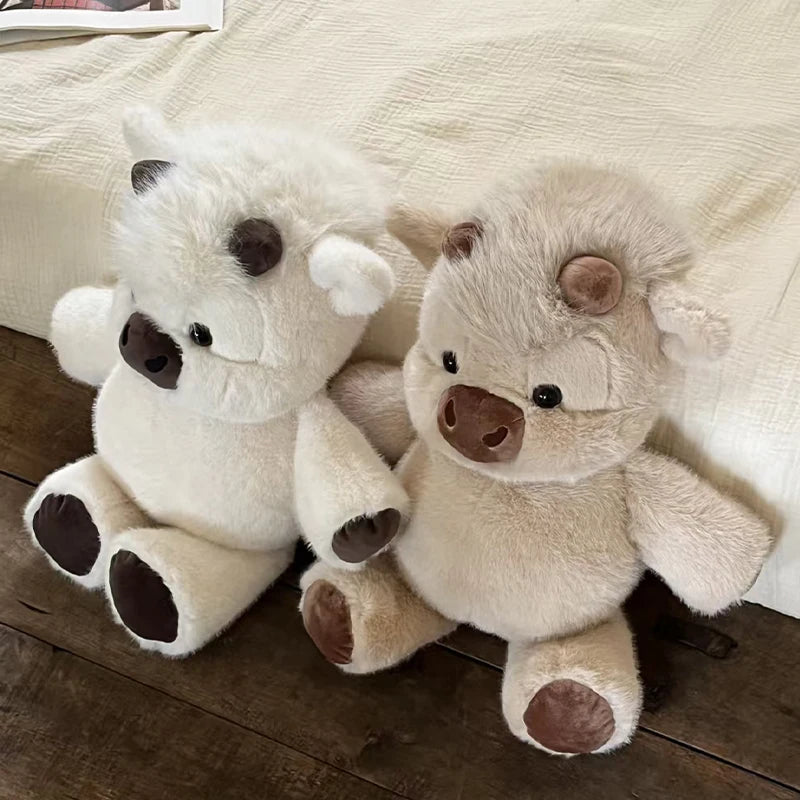 Jouet en peluche blanc et duveteux d'un veau écossais avec des accents bruns, posé sur un tissu clair.