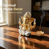 Golden Ganesha statue figurine with a lit incense stick and a lotus flower on a wooden table.